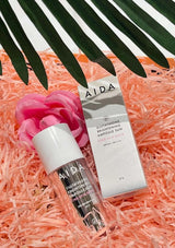 AIDA skincare product packaging on pink shredded paper with a palm leaf in the background