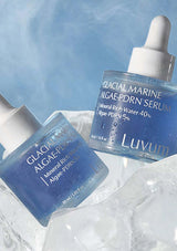 Two bottles of Luvum Glacial Marine Algae-PDRN Serum on a textured white surface with a blue gradient background.