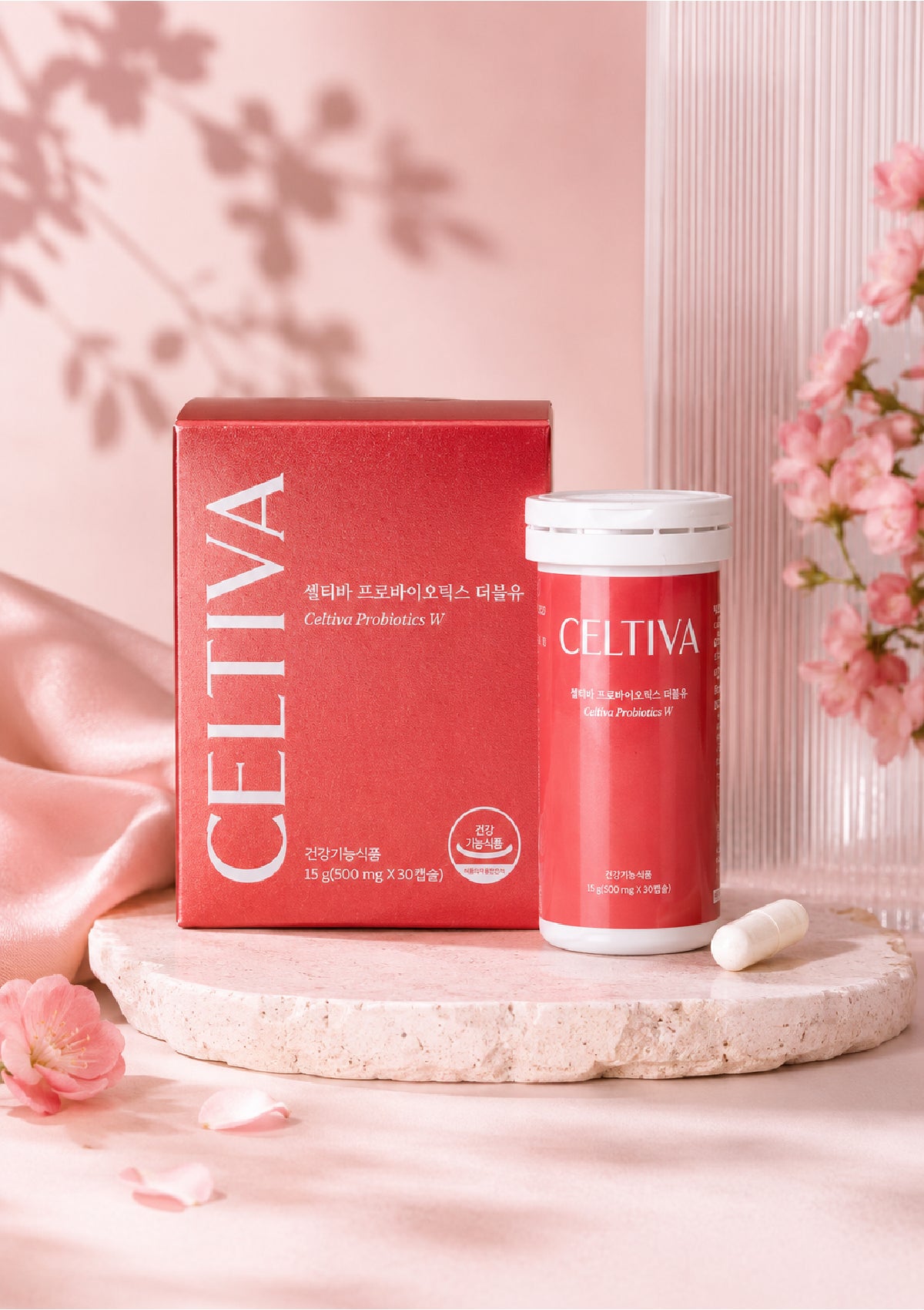 Celtiva Cellulose Probiotic supplement shown with its red product box and matching red bottle on a stone slab, styled with pink flowers and soft pink fabric in a clean studio setup.