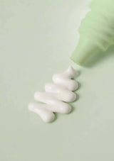 Green bottle dispensing white cream on a light green background