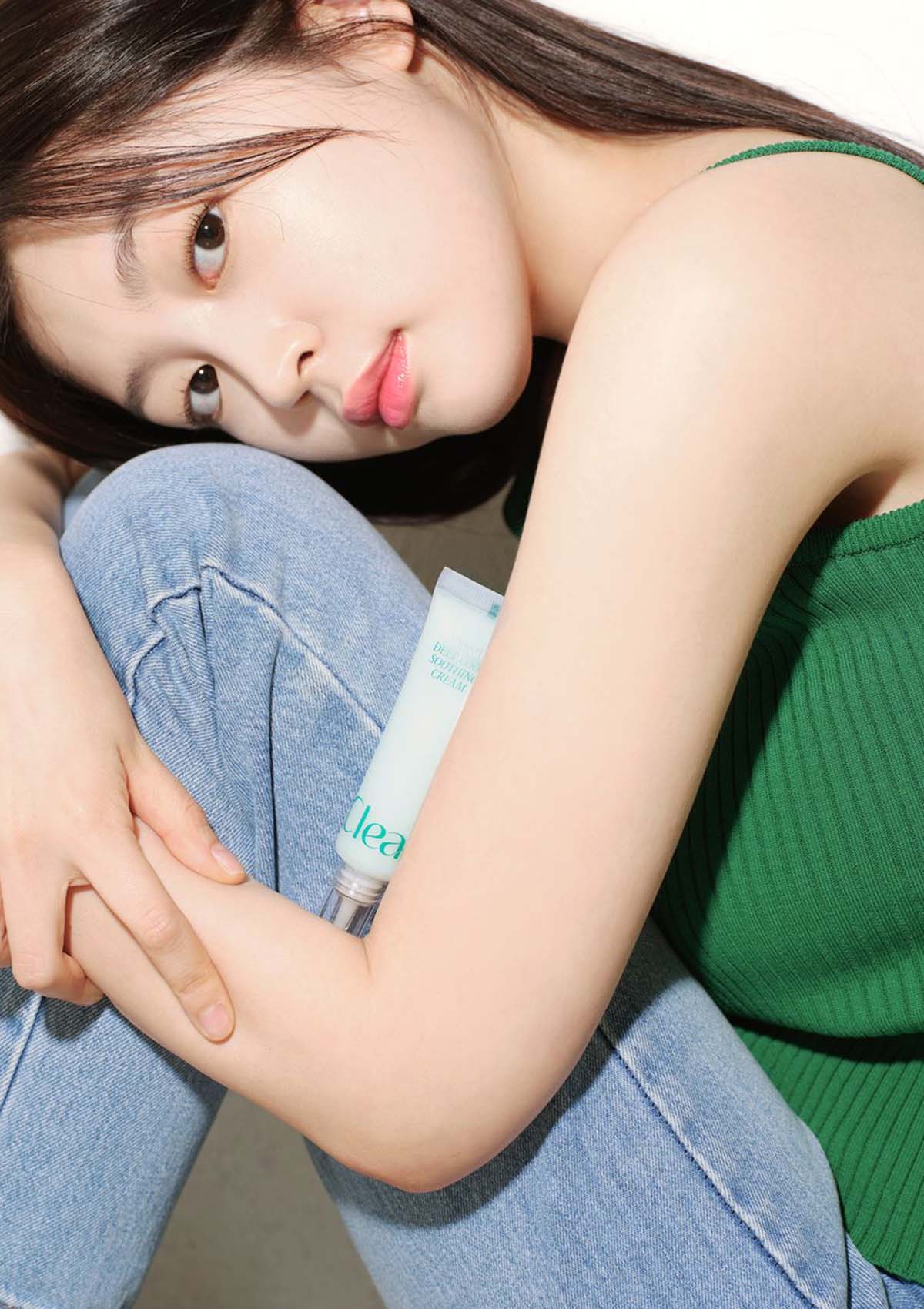 Woman holding a bottle of 'Clear' skincare product with a neutral background