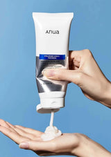 Hand holding a tube of Anua skincare product with blue background