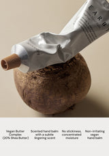 Hand balm tube being squeezed onto a textured surface with product details below.