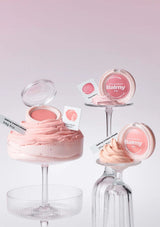 Pink makeup products on glass stands with 'Balmy' branding on a light pink background