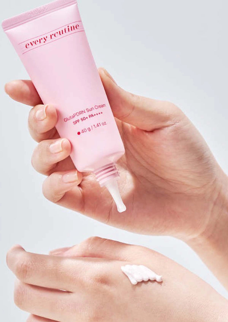 Hand holding a pink skincare tube labeled 'every routine' with a small amount of cream on the palm.
