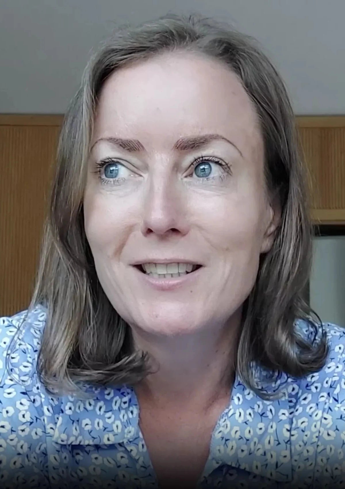 Woman with blue eyes and brown hair wearing a blue floral top.
