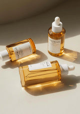 Three bottles of a skincare product with droppers on a beige surface