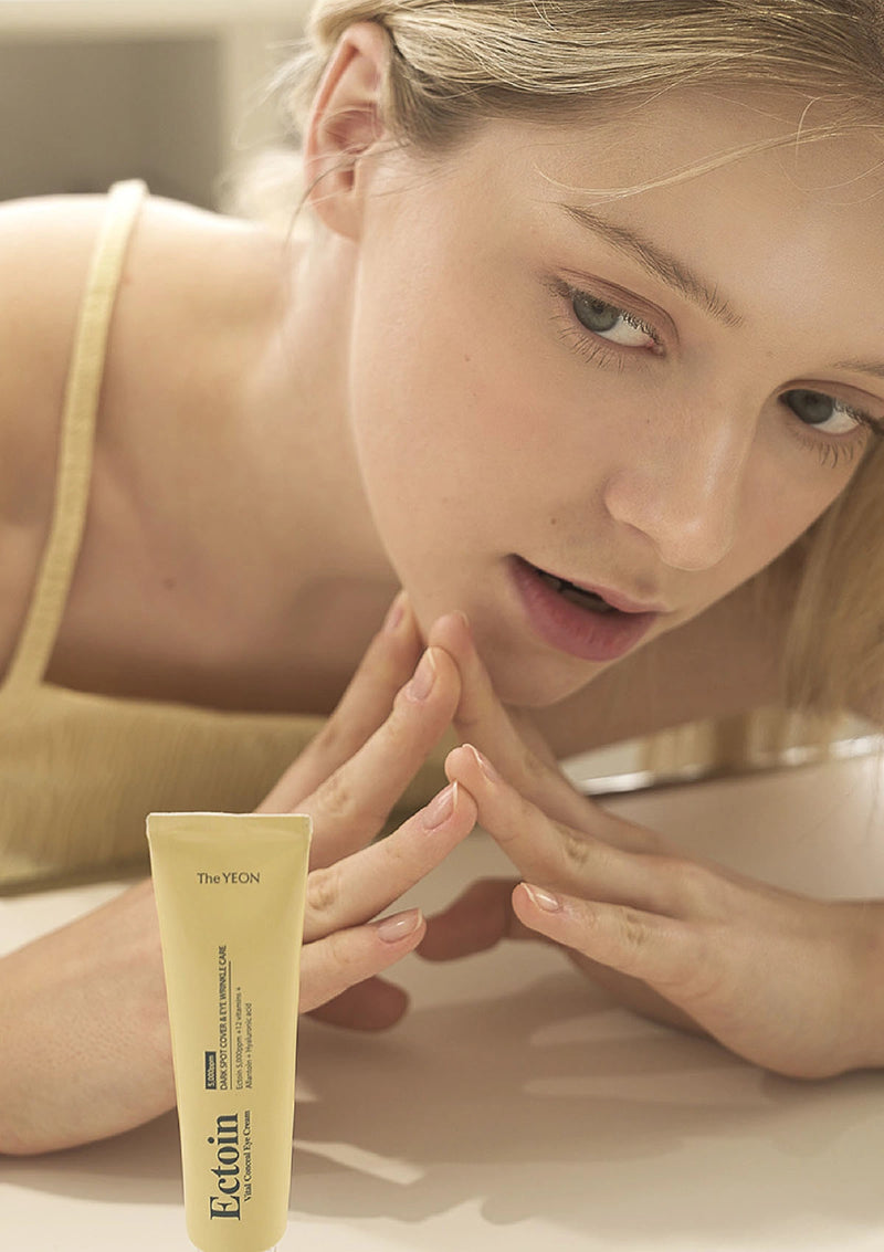 Woman applying cream to her face with a tube of cream in front of her.