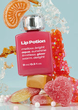Pink lip balm labeled 'Lip Potion' surrounded by colorful candy on a light blue background