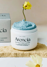 Arencia Royal Blue Hydrating Cleanser with a yellow flower on top, placed on a beige surface.