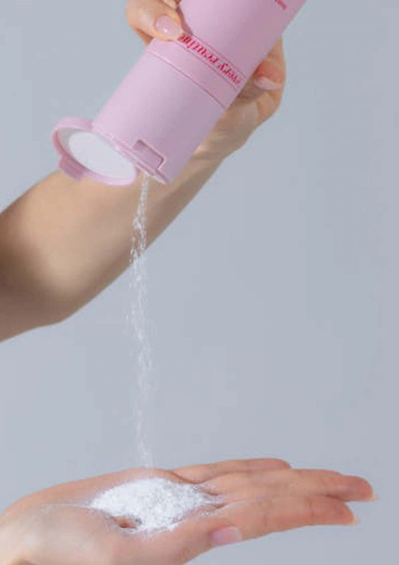 Person using a pink powder puff to apply white powder to their hand against a gray background