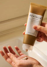 Person holding a tube of Madapical Centella Ampoule Foam over their palm with a neutral background