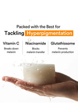 A hand holding a translucent white bar of skincare cream with water droplets splashing off it, set against a white background with text highlighting key ingredients: Vitamin C, Niacinamide, and Glutathione.