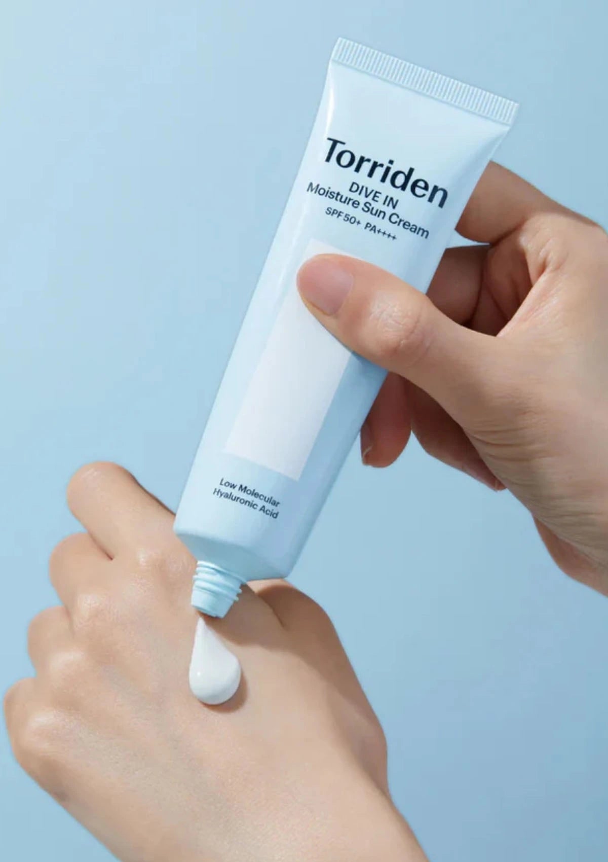 Hand holding a tube of Torriden skincare product against a light blue background