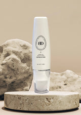 White skincare bottle with 'BD' logo on a stone surface against a beige background
