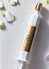 White and gold cosmetic syringe with 'Ellegance' branding on a light gray background with white flowers.