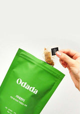 Green Odada package with a hand holding a sachet of tea.