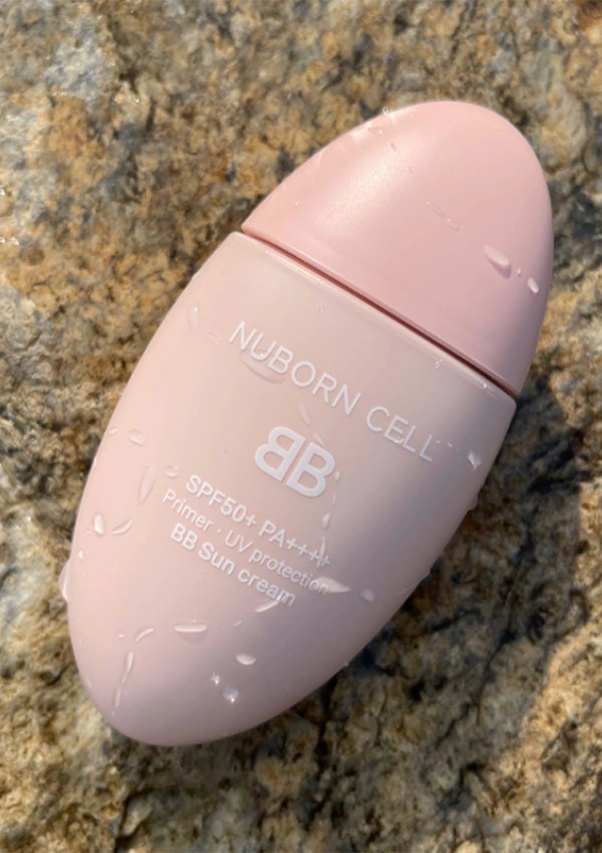 Pink BB cream bottle labeled 'Nuborn Cell' on a textured stone background