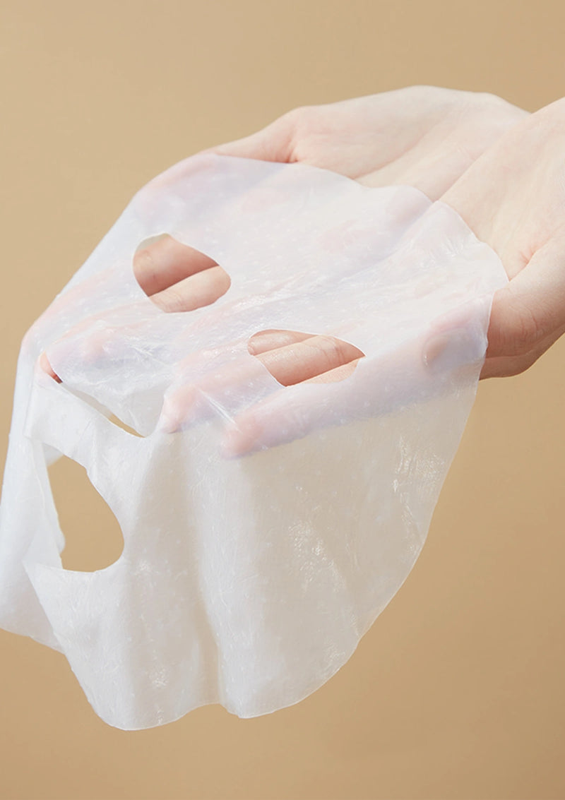 Sheet mask held by a hand against a beige background