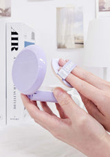 Hand holding a small purple device with a white strap on a blurred magazine background