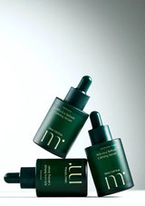 Three green skincare bottles with droppers on a gradient background