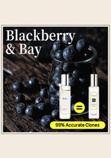 Perfume bottles with blackberries on a wooden surface, labeled 'Blackberry & Bay'.