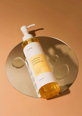 Bottle of cleansing oil with a pump on a gold circular tray against an orange background