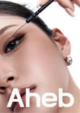 Close-up of a woman's face with dramatic eye makeup while a hand applies false eyelashes with a lash pen. Large white text 'Aheb' appears at the bottom on a white background.