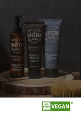 Bartera grooming products including a pump bottle, tube of cream, and tube of cleansing foam on a wooden block with a dark background.