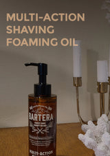 Bartera multi-action shaving foaming oil bottle on a wooden surface with candles in the background.