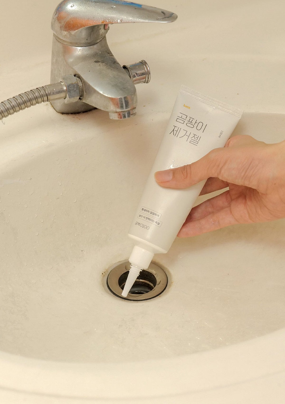 Hand using a tube of white cream to unclog a sink drain.