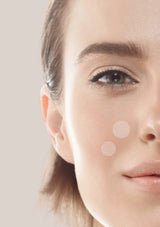 Close-up of a woman's face with two dots on her cheek against a neutral background