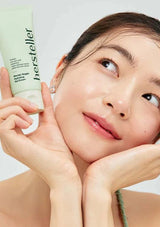 Woman holding a tube of hersteller skincare product against a plain background