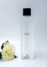 Bottle of 'Beauty Water' with a black cap on a white background, featuring a white flower.