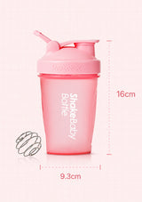 Pink Shakebaby shaker bottle with a flip-top lid, shown on a pale pink background with dimension markings of 16 cm height and 9.3 cm width, plus a small metal whisk attachment.