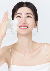 Woman applying a white patch to her face against a plain background