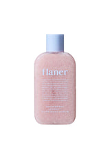 Pink bottle of Flaner body scrub with a blue cap on a white background