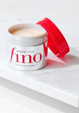 Open jar of 'fino' hair mask with red cap on a white background