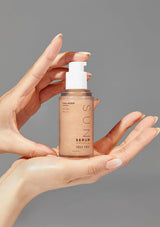 Hand holding a bottle of SUN serum with a gray background