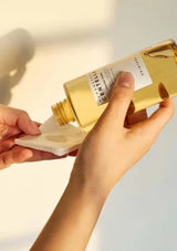Hand holding a gold bottle of Centrum skincare product with a blurred background