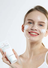 Woman with a skincare product on her face and holding a bottle against a white background