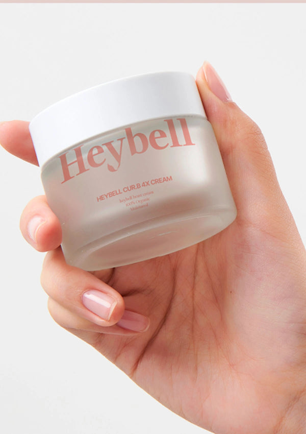 Hand holding a jar of Heybell cream against a white background