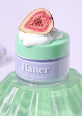Green jar of flaner fig pudding repair cream with a slice of fig on top against a light purple background