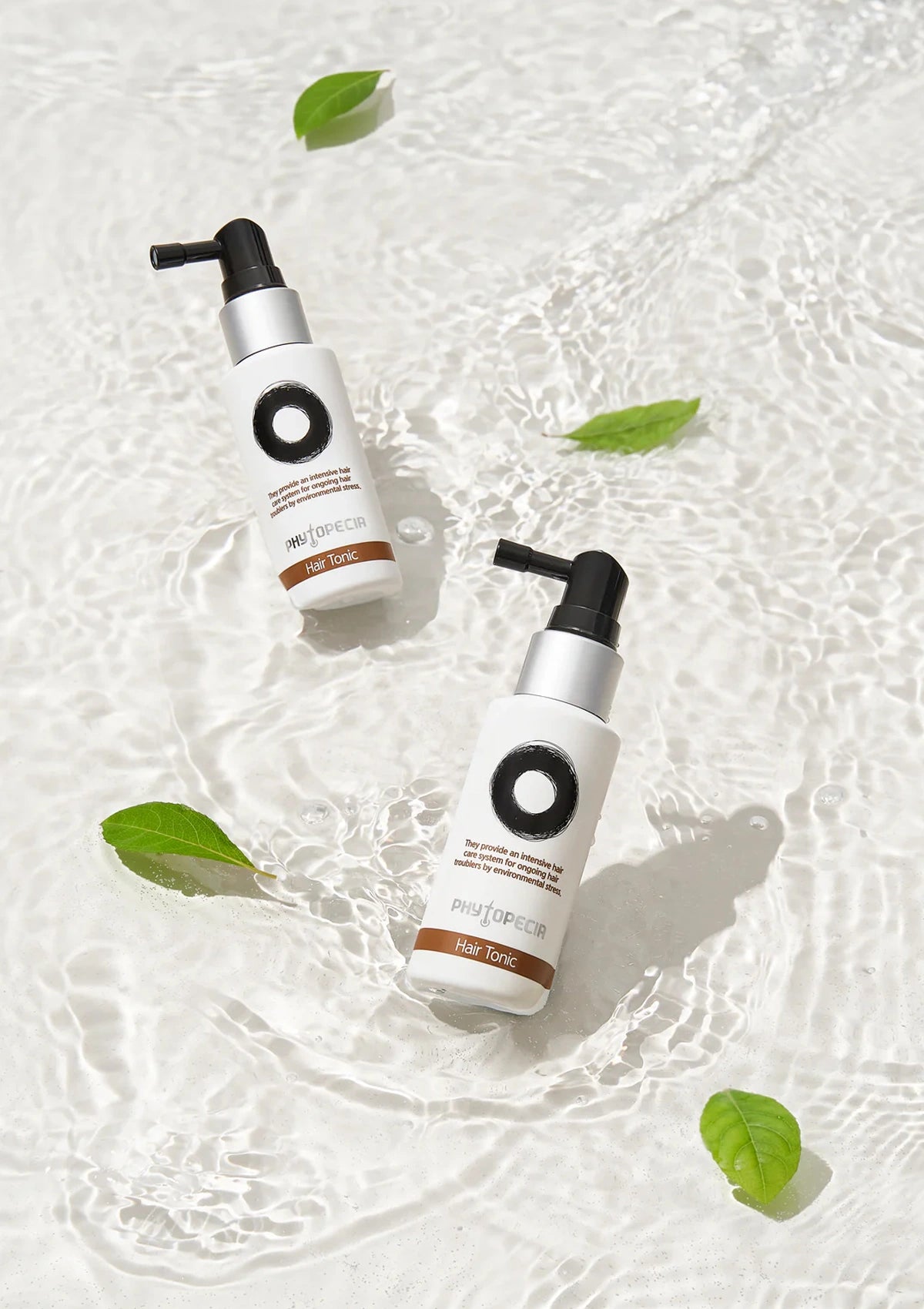 Two skincare bottles with green leaves on a textured white background