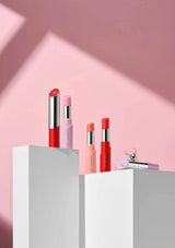 Set of lipsticks on a white pedestal against a pink background