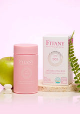 Pink Fitany supplement container and box with green apple and white pills on a light pink background