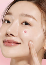 Woman applying cream to her face with a pink background