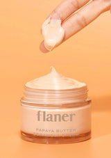 Jar of flaner Papaya Butter Ceramella Cream with a hand applying cream on an orange background