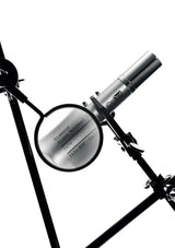 A close-up studio shot of a silver cylindrical product mounted on a black stand, with a circular magnifying glass or lens showing engraved text on a white background.