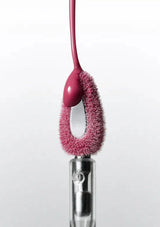Pink cleaning brush with bristle head attached to a clear cylindrical handle on a white background